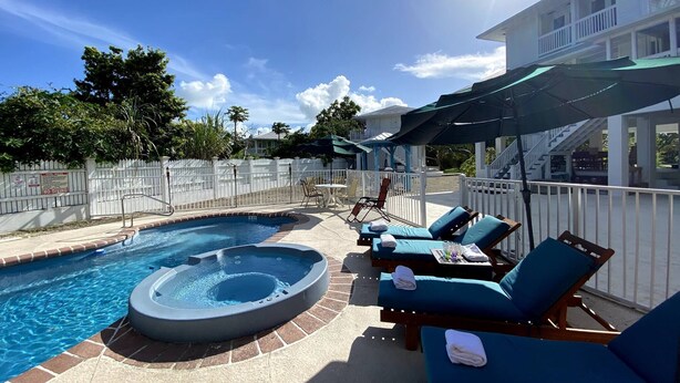 Un área de piscina con jacuzzi, sillones de descanso y sombrillas.