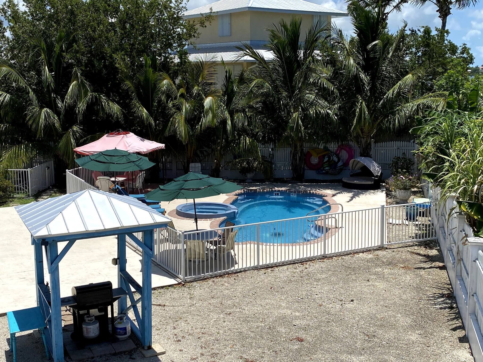 Una piscina con un'area recintata, circondata da palme e una recinzione bianca.