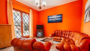 Een woonkamer met oranje wanden, een grote bank, een salontafel en een televisie.