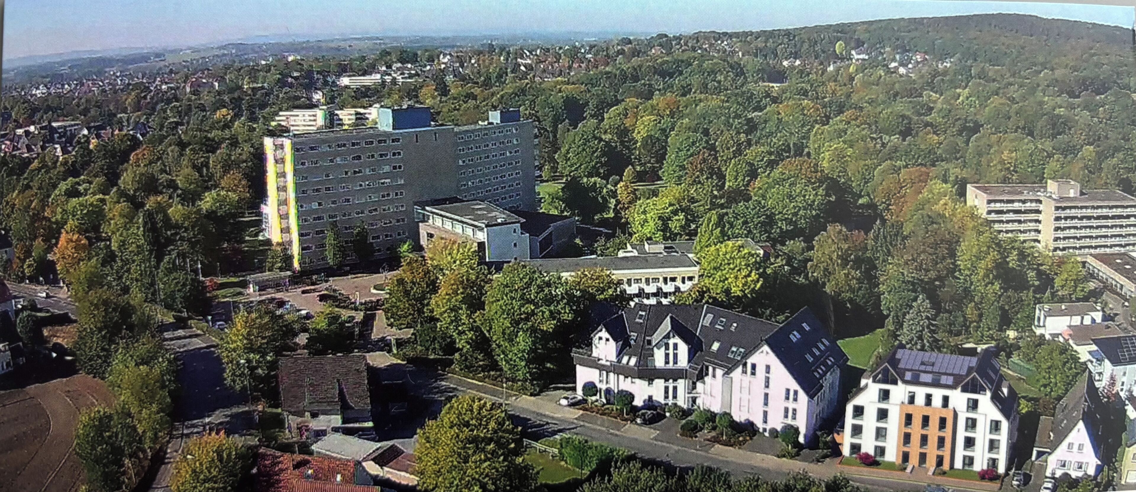 Vista aérea de una zona residencial con una mezcla de edificios modernos y tradicionales, rodeada de abundante vegetación.