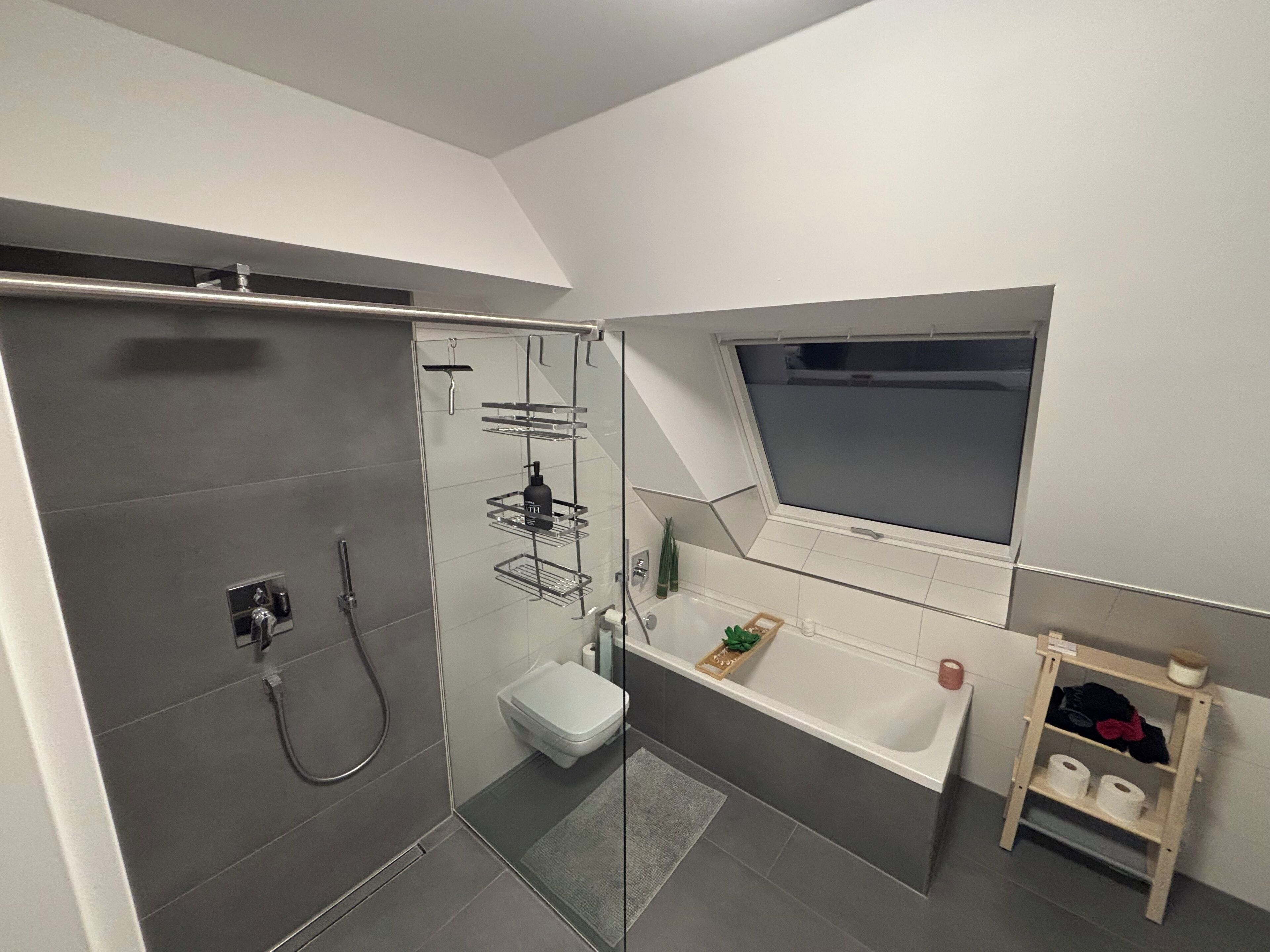 A modern bathroom with a glass-enclosed shower, a toilet, a bathtub, and a small window.