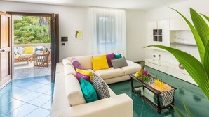 Een moderne woonkamer met een bank, salontafel en uitzicht op een balkon met tuinmeubilair.
