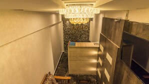 A modern bathroom with a marble floor, a wooden vanity, a chandelier, and a stone wall backsplash. - Hotel Fortune Elite (Mumbai)