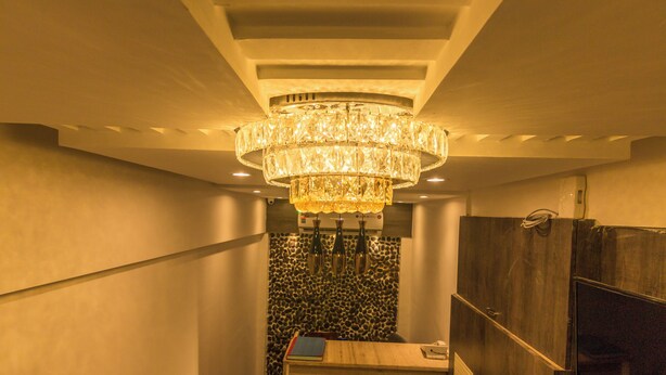 A modern interior with a large crystal chandelier, a wooden reception desk, and a patterned wall. - Hotel Fortune Elite (Mumbai)