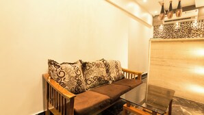 A modern living room with a wooden sofa, patterned cushions, a glass coffee table, and a stone accent wall. - Hotel Fortune Elite (Mumbai)