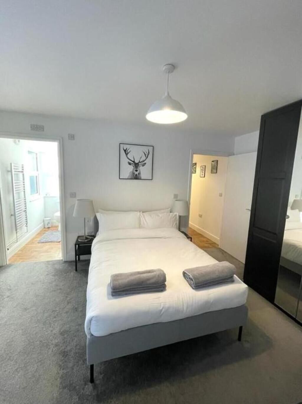 A neatly made bed with folded towels, a wall-mounted picture of a deer head, and a pendant light.