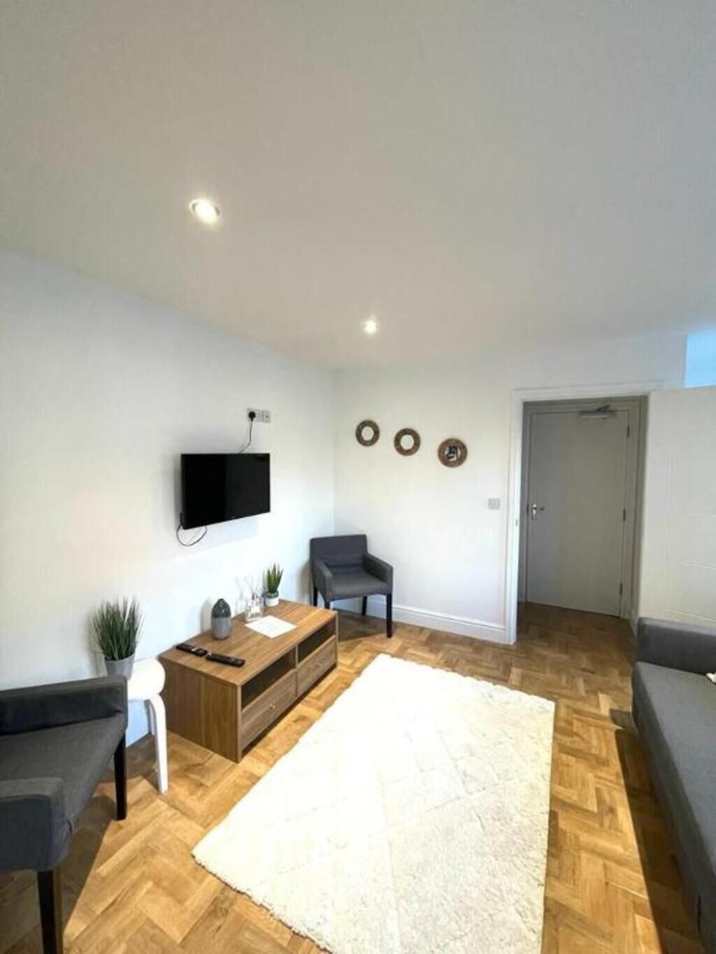 Een moderne woonkamer met een flatscreen televisie, een grijze bank, een houten salontafel en een witte vloerkleed.