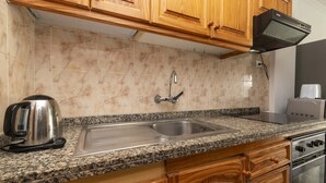 Eine Küche mit Holzschränken, einer Granitabdeckung, einem Edelstahlspülbecken, einem Wasserkocher und einem Toaster.