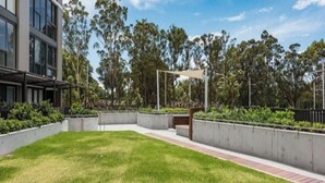 Un edificio moderno con un cortile erboso, fioriere in cemento e cielo sereno.