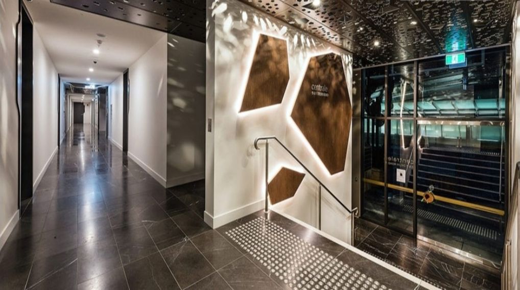 A modern hotel lobby with a sleek design, featuring a central wall with geometric patterns and a glass elevator.