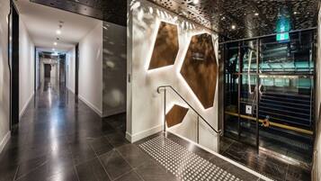 A modern hotel lobby with a sleek design, featuring a central wall with geometric patterns and a glass elevator.