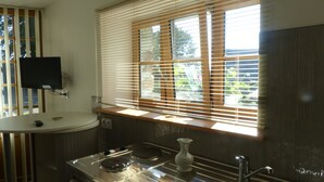 A kitchen with a stove, sink, and window with blinds. - Demeure des tilleuls (Locquénolé)