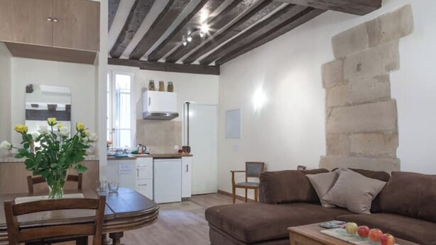 Un salon chaleureux avec un canapé marron, une table à manger avec des chaises et un coin cuisine doté d’un réfrigérateur blanc et de placards.