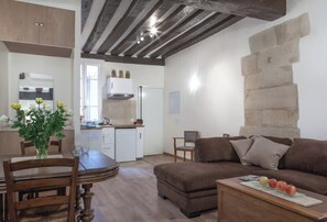A cozy living room with a brown sofa, a dining table with chairs, and a kitchen area with a white refrigerator and cabinets. - Beautiful apartment Louvre Center (paris)