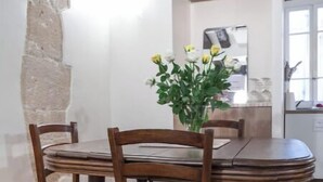 Un coin repas avec une table et des chaises en bois, un vase de fleurs et un mur en pierre.