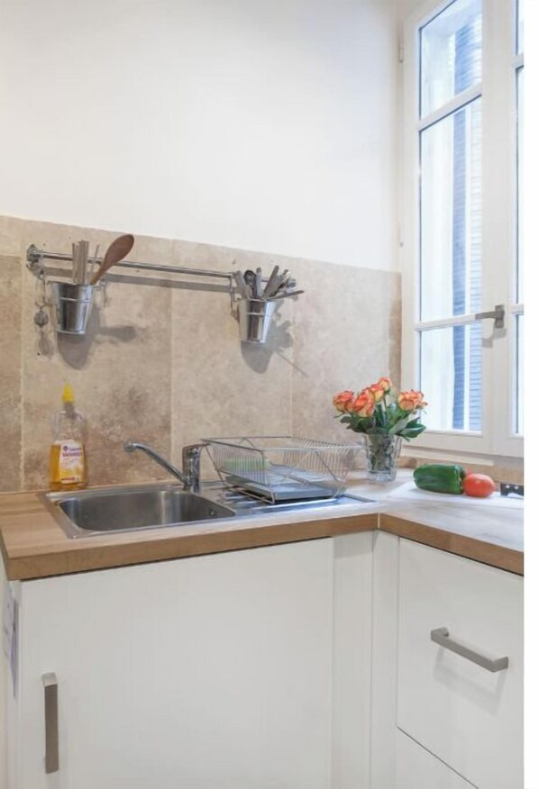 A kitchen with a stainless steel sink, a dish rack, and a window with blinds. - Beautiful apartment Louvre Center (paris)
