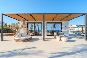 A covered outdoor seating area with a wicker chair, white cushions, and a view of the sea. - Nysa Luxury villa 3,Private pool,Near Hersonissos (Heraklion)
