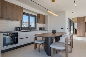 A modern kitchen with built-in appliances, a dining area with a round table and chairs, and a view through a window. - Nysa Luxury villa 3,Private pool,Near Hersonissos (Heraklion)
