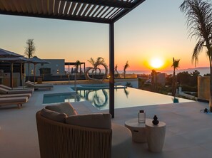 A poolside area with lounge chairs, a small table, and a view of the sunset over the ocean. - Nysa Luxury villa 3,Private pool,Near Hersonissos (Heraklion)