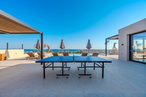 Tafeltennistafel op een dak met lounge stoelen en parasols, met uitzicht op de kust.