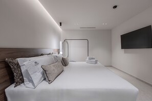 A modern hotel room with a neatly made bed, a flat-screen TV mounted on the wall, and a minimalist design. - Nysa Luxury villa 4, Private pool, Near Hersonissos (Heraklion)