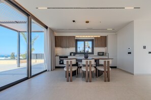 A modern kitchen with a dining area, large windows, and a view of the sea. - Nysa Luxury Villa 5 ,Private Pool near Hersonissos (Heraklion)