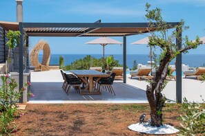 A covered outdoor seating area with a table and chairs, a pergola, and a view of the sea. - Nysa Luxury Villa 5 ,Private Pool near Hersonissos (Heraklion)