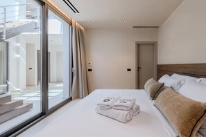 A modern hotel room with a large bed, a view of a staircase, and a door leading to another room. - Nysa Luxury Villa 5 ,Private Pool near Hersonissos (Heraklion)