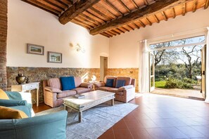 Un soggiorno con parete in pietra, travi a vista in legno, un divano, un tavolino da caffè e vista sull'esterno.