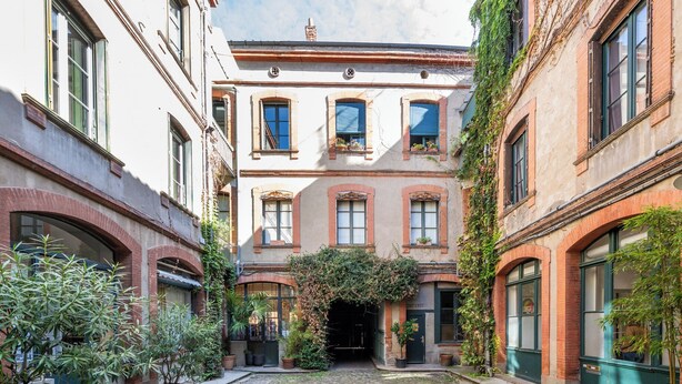 Um pátio com chão de pedras, rodeado por edifícios com janelas em arco e fachadas de tijolo.