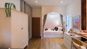 Quarto com cama, escrivaninha, guarda-roupa e porta para outro espaço.