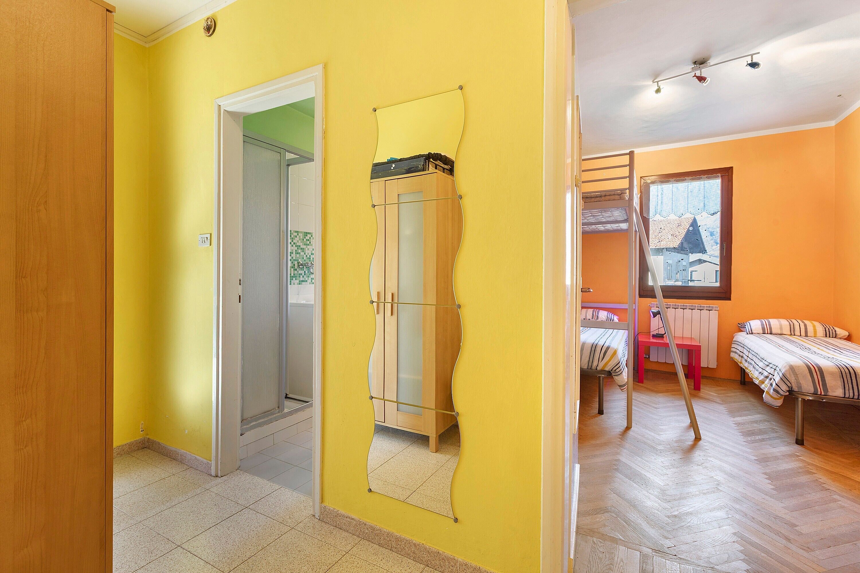 Ein Zimmer mit einem Holzschrank, einem Spiegel, einem Bett mit gestreifter Bettwäsche und einem Fenster mit Blick auf Gebäude.