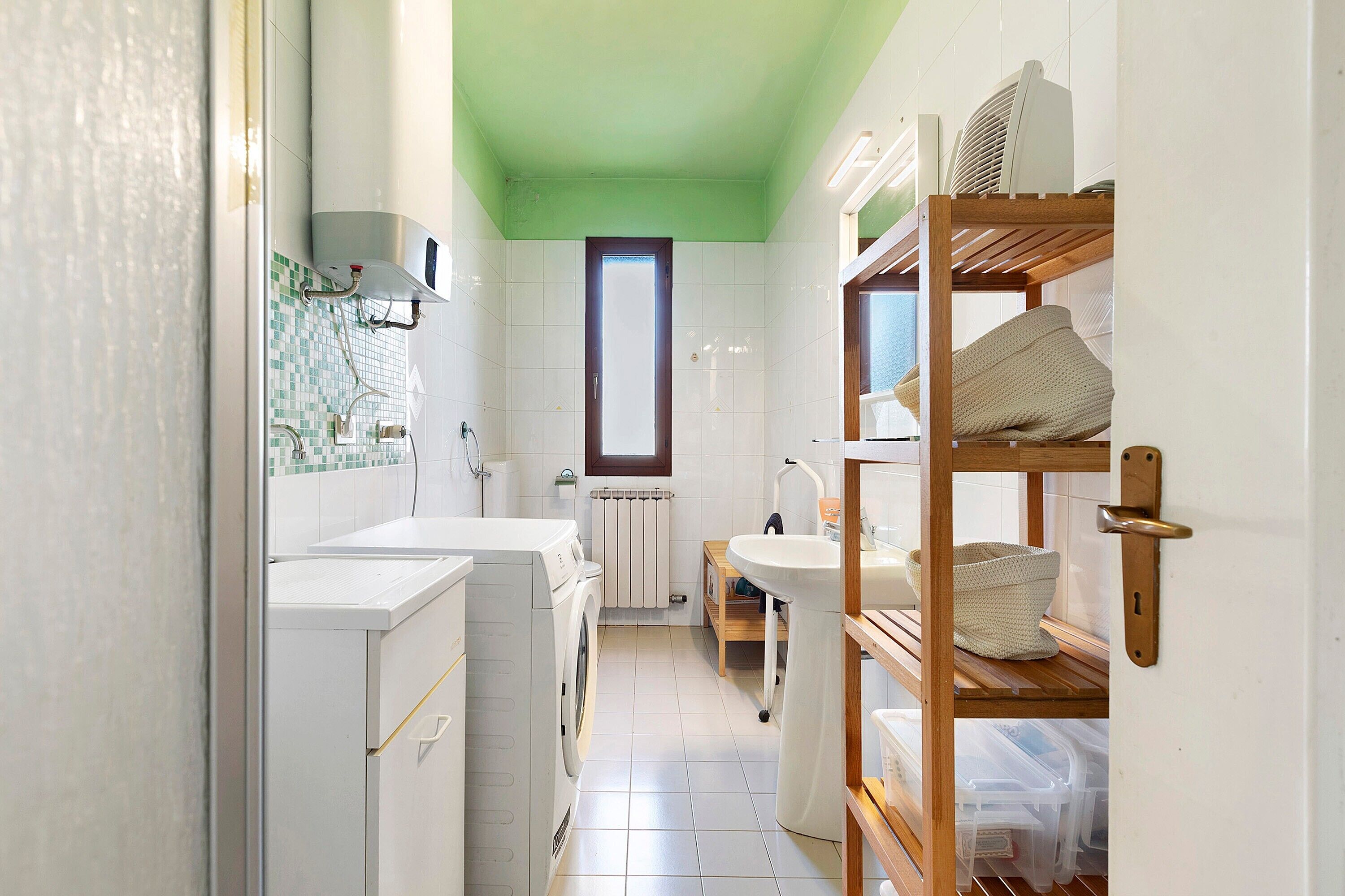 A compact, modern bathroom with a washing machine, a sink, and a wooden shelf.
