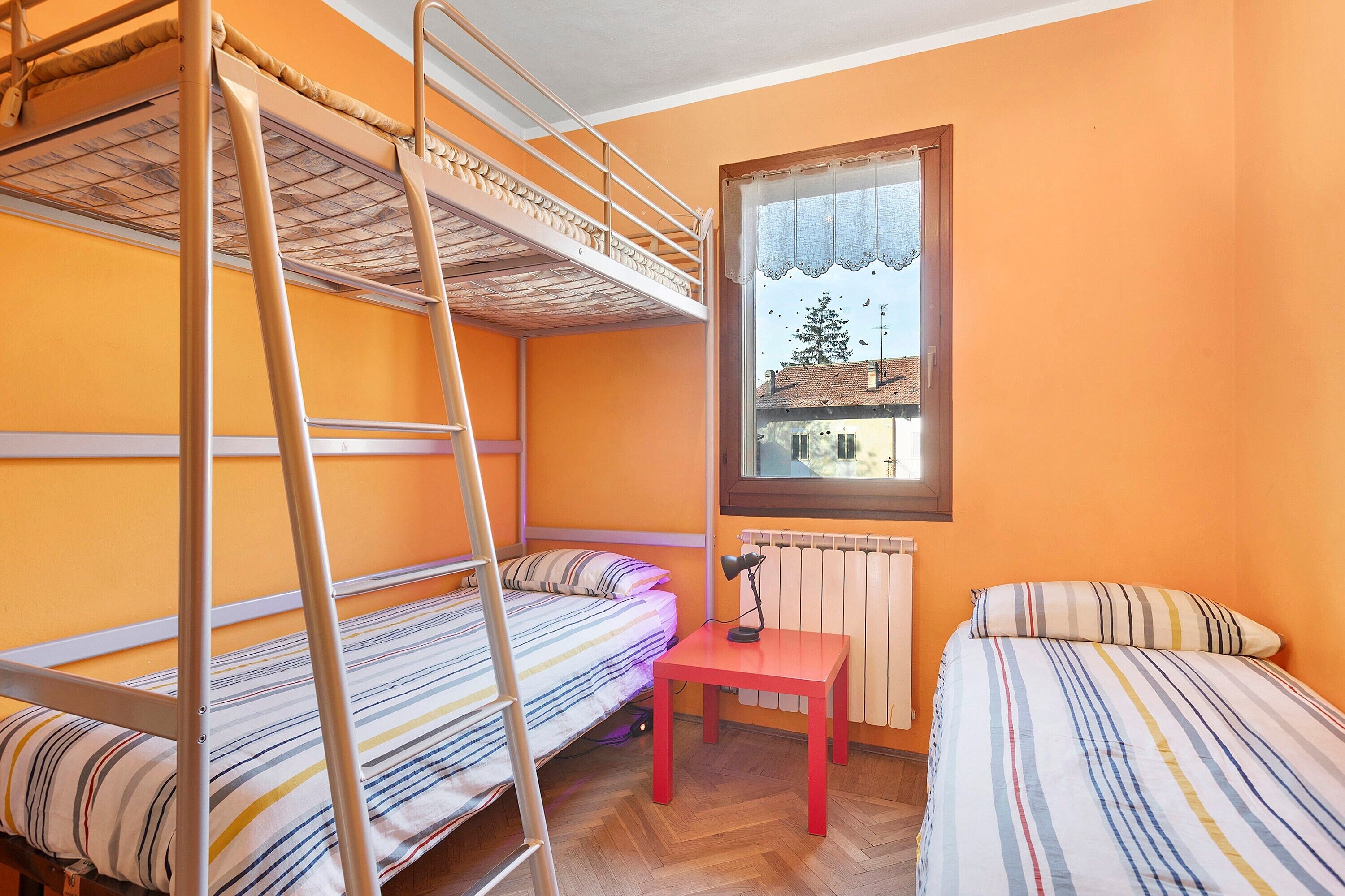 A dormitory room with bunk beds, a small table, and a window with a view.