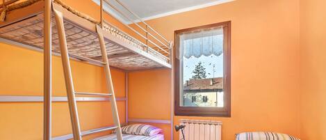 A dormitory room with bunk beds, a small table, and a window with a view.
