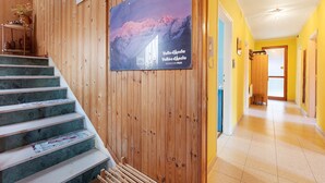 Een trap met een houten wand en een poster, een gang met gele muren, en een deur die naar een andere kamer leidt.