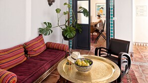 A cozy living room with a sofa, a round coffee table, and a chair. There is a potted plant and a bowl of fruit on the table. - Andalusian Villa with moorish touch and "Hammam" pool (Granada/Albuñol/La Rábita)