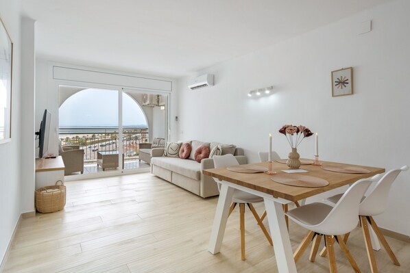 Ein modernes Wohnzimmer mit einer Couch, einem Esstisch und Stühlen. Ein großes Fenster bietet Blick auf die Stadt.