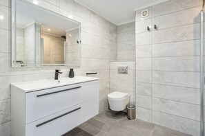 Ein modernes Badezimmer mit einem weißen Waschtisch, einem großen Spiegel, einer Toilette und einer Duschkabine.
