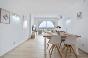 Ein moderner Essbereich mit einem Holztisch, weißen Stühlen und Blick auf das Meer durch große Fenster.