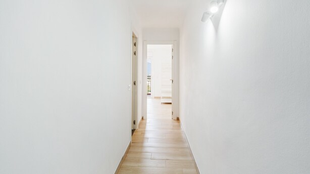 A narrow, well-lit hallway with wooden flooring and white walls, leading to an open space. - Welcs Apartamento 064 EMP Frente al Mar (Castello d'Empuries)