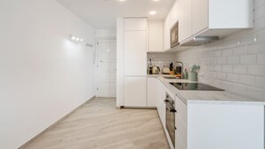 A modern kitchen with white cabinetry, a built-in oven, and a countertop with a kettle and other appliances. - Welcs Apartamento 064 EMP Frente al Mar (Castello d'Empuries)