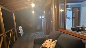 A wooden deck with a sofa and cushions, a glass door leading outside, and a metal railing on one side. - Sítio Solar di Stella (Itatiaia)