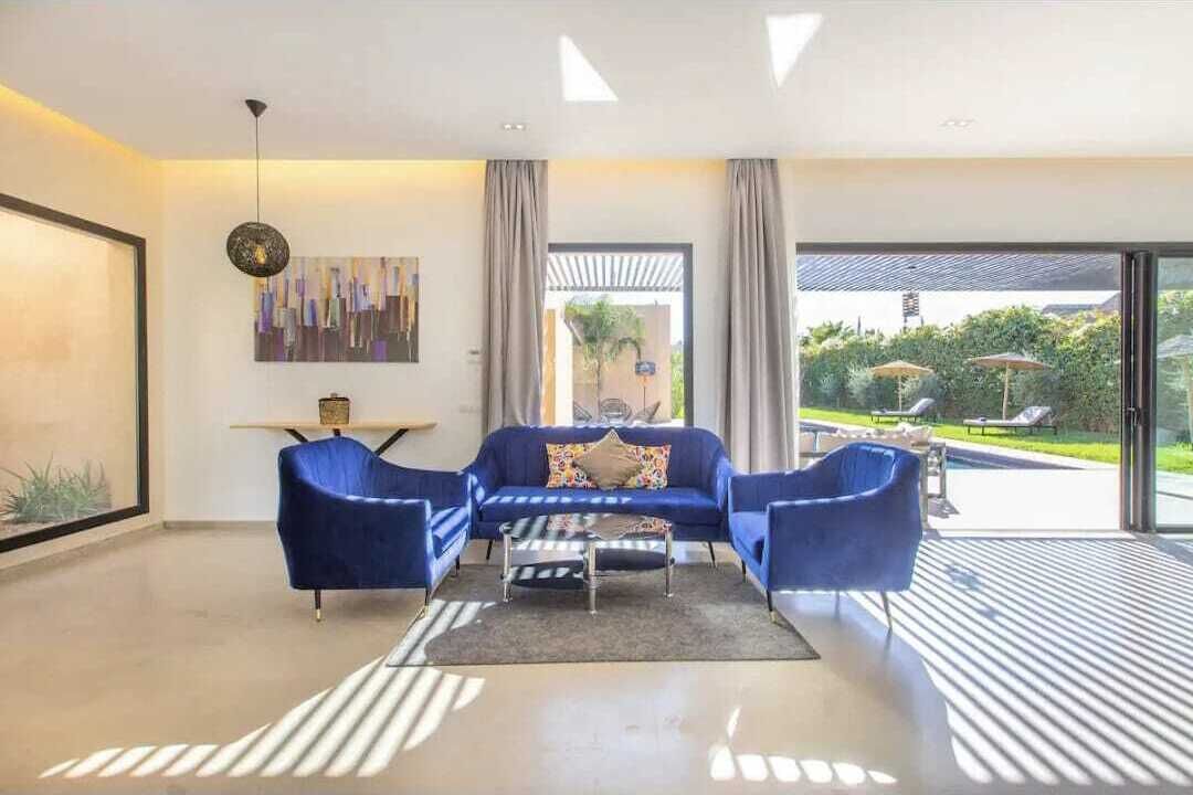 Una sala de estar moderna con un sofá azul, una mesa de centro y vistas a una piscina y jardín.