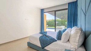Een moderne slaapkamer met een groot bed, blauwe gordijnen en uitzicht op groen.