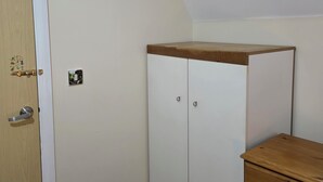 Una habitació amb una porta de fusta, un armari blanc, un petit calaixera de fusta i un gresol.
