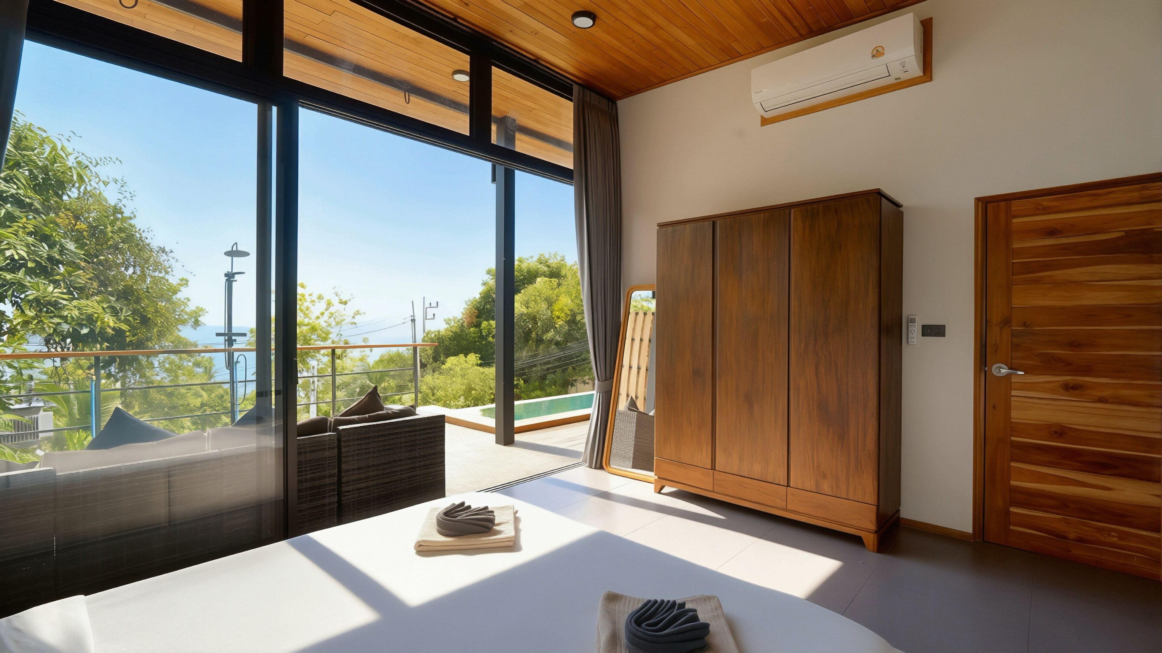 Ein Schlafzimmer mit großen Fenstern, einem Holzschrank und Blick ins Grüne.