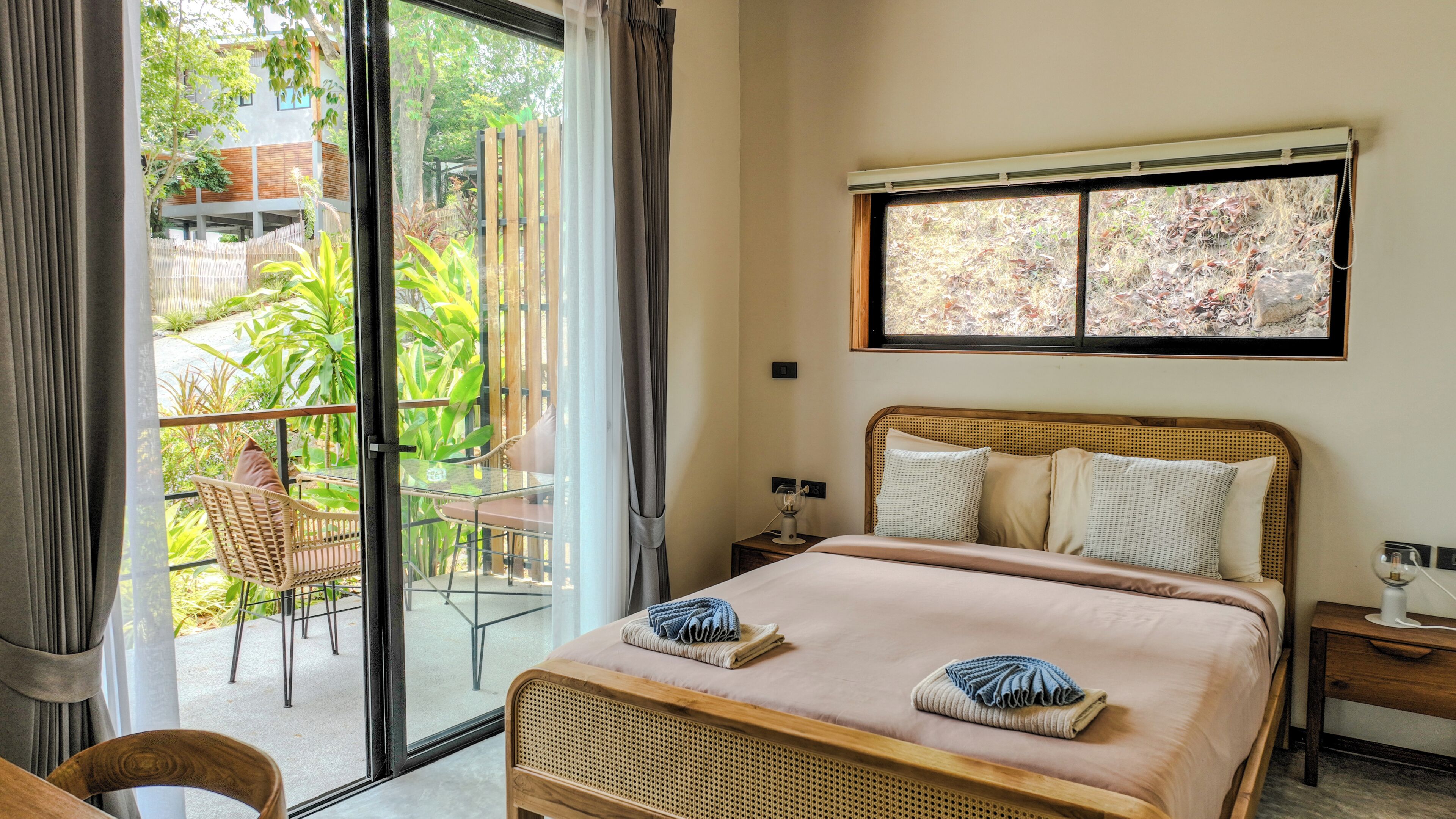 Habitación de hotel con cama, una mesita, una silla, ventana con vistas a zonas verdes y un balcón.