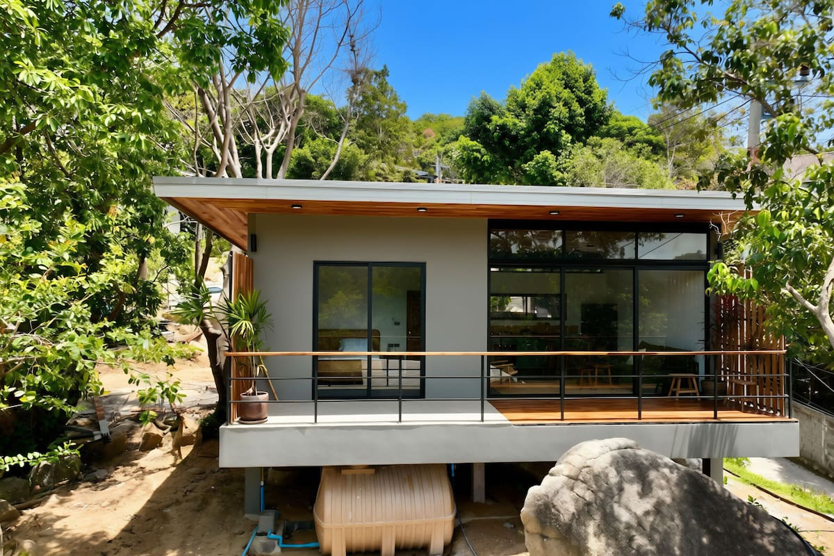 Una casa moderna con balcón, ventanas amplias y una terraza de madera.