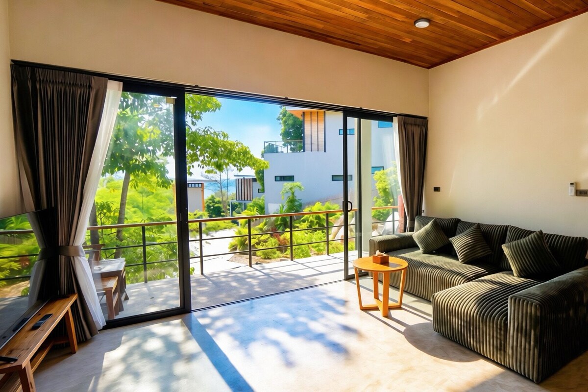 A modern living room with a sofa, a small table, and a view of a balcony with a railing.